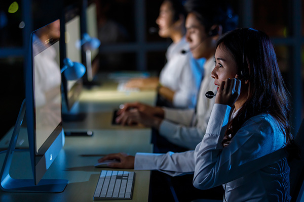 Call center agents wearing headsets working at their computers in a dimly lit office, providing safety network services and emergency assistance.