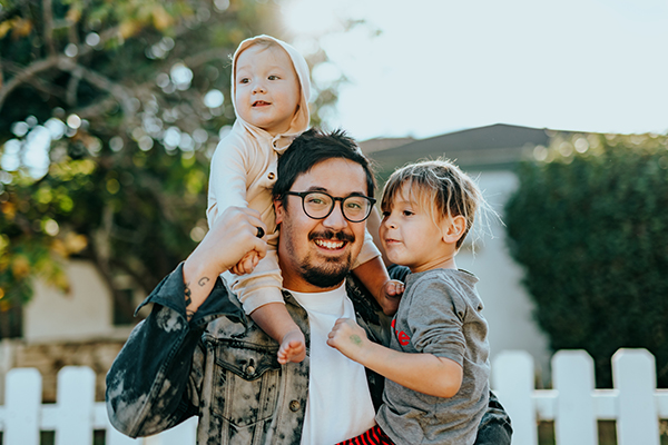 Smiling father with two children in front of white picket fence