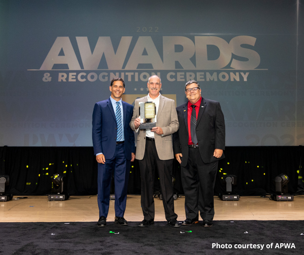 Three people standing on stage with background that reads "2022 Awards & Recognition Ceremony." Joseph Ouellette from CTDOT is in the center and holds Professional Manager of the Year in Transportation Award from the APWA