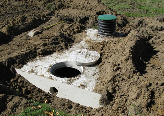 Concrete septic tank buried in dirt and partially exposed.
