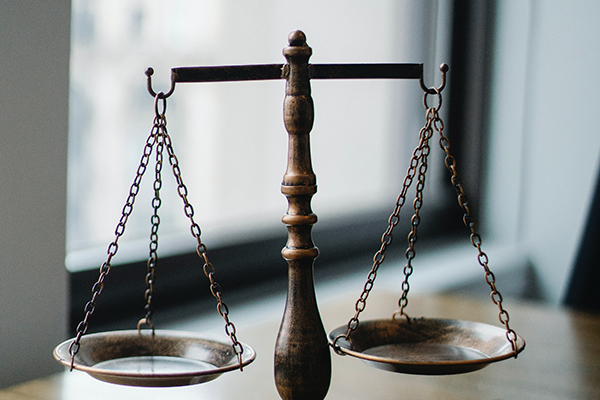 Bronze justice scale next to window on desk.