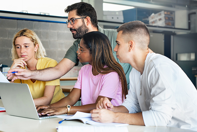 A teacher points to a computer screen as three students look on