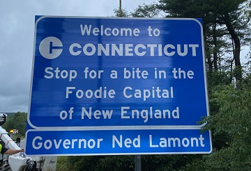 Interstate highway sign that says, "Welcome to Connecticut, Stop for a bite in the Foodie Capital of New England"