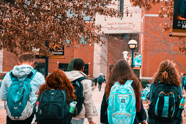 Backside view of a group of students walking towards a school.