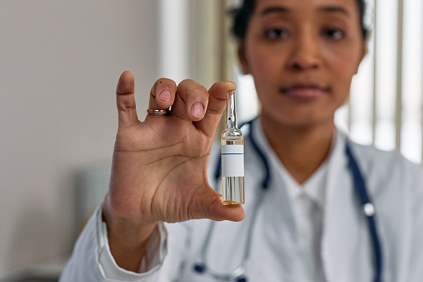 Close up shot of healthcare professional in white lab coat holding an ampoule of vaccine medicine.