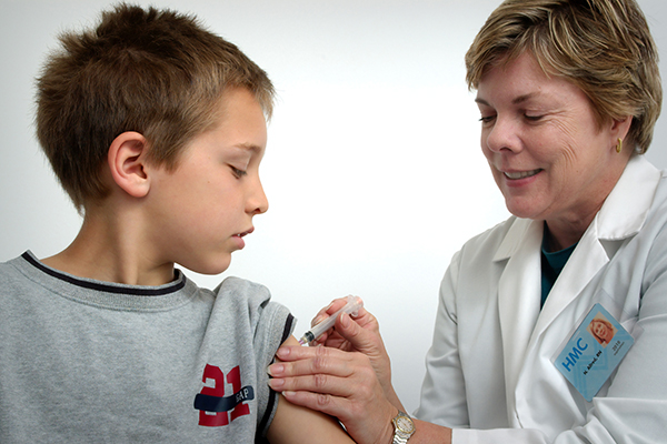 Healthcare worker giving vaccine shot to young boy in his arm.