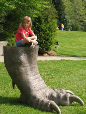 Girl sitting on enlarge dinosaur foot at Dinosaur State Park.