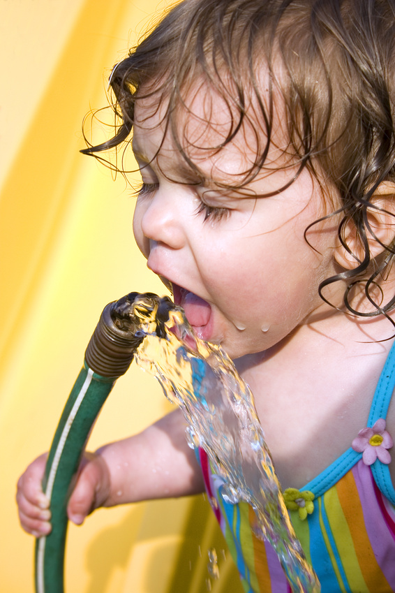 Toddler in a bathing suit drinking out of water hose