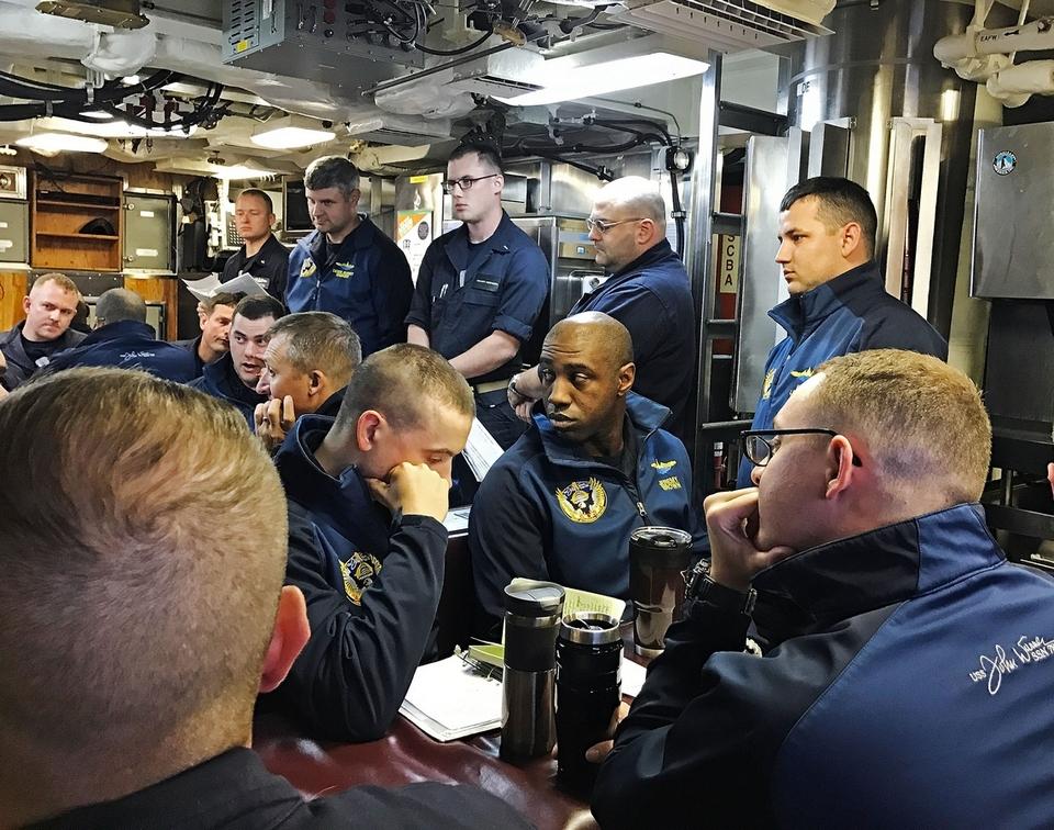 Crewmembers take part in a piloting briefing in the crew's mess aboard the USS John Warner.