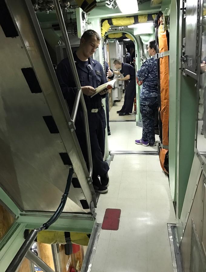 A sailor reads while waiting to go through the chow line aboard the USS John Warner.