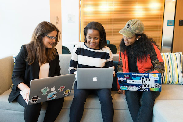 three women sitting in a row, typing on laptops