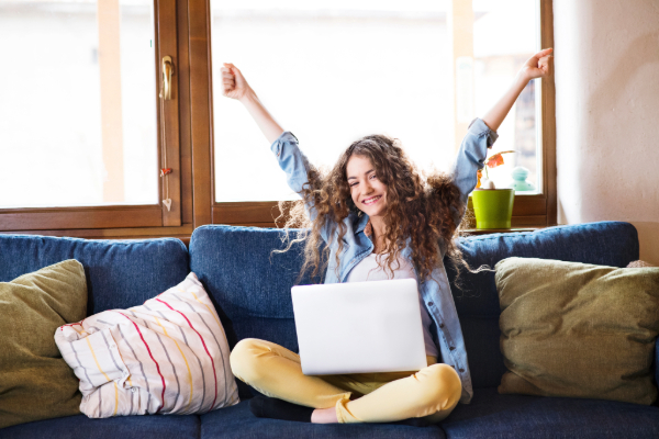 Happy woman sitting on couch with laptop on her lap. 