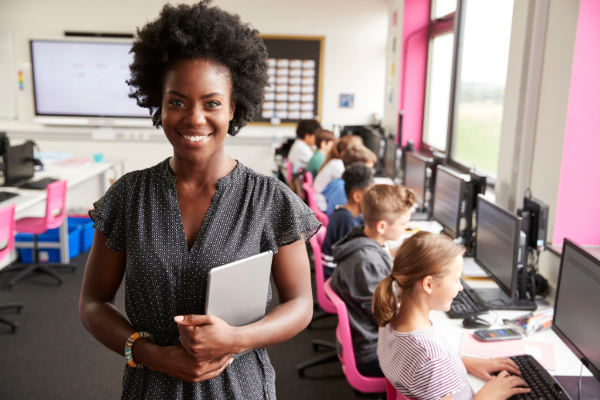 Woman teacher standing in front of students sitting at computers