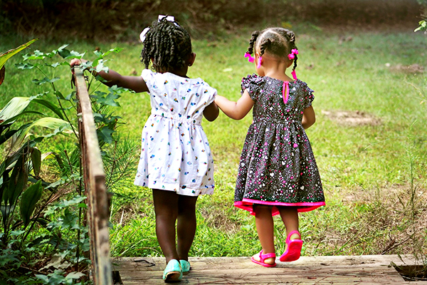 Two young children crossing a small bridge in a garden.