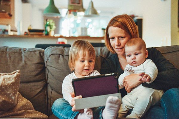 Caucasian mother sitting with two children on couch in front of tablet.