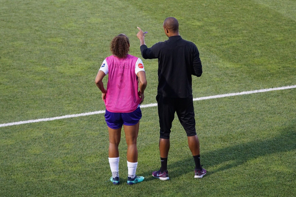 male soccer coach talking to female player on the sideline
