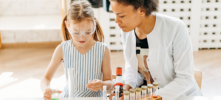 adult woman and young girl work together on a science project with test tubes and a microscope