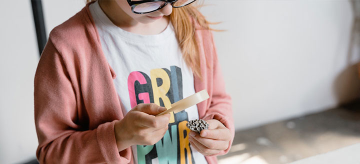 elementary student using a magnifying glass while wearing a girl power shirt